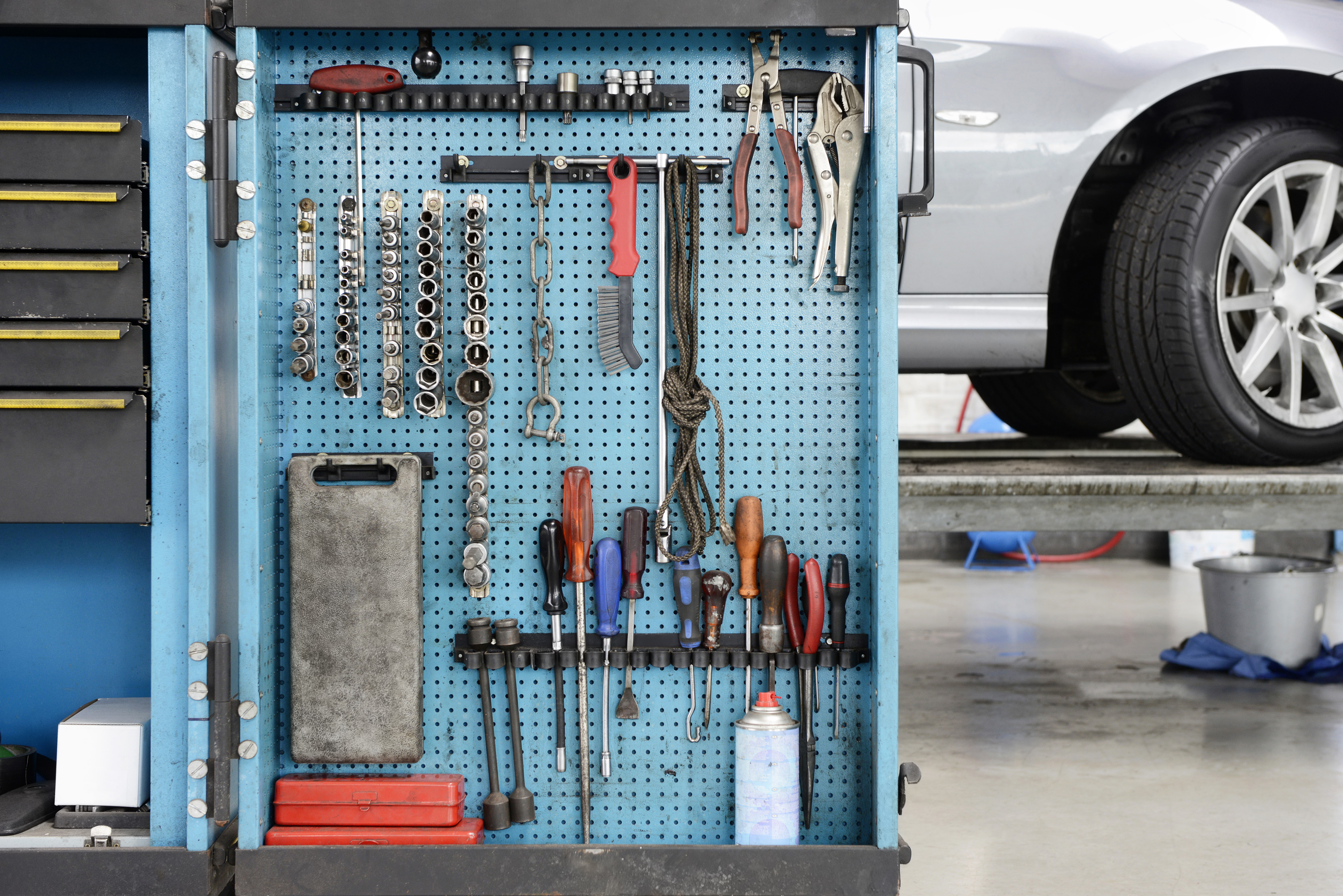 Tools on a blue board in a storage cabinet,organised in rows,at an auto repair shop.
